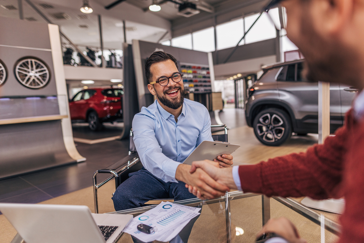 two men shaking hands at a car dealership. Buying and selling cars